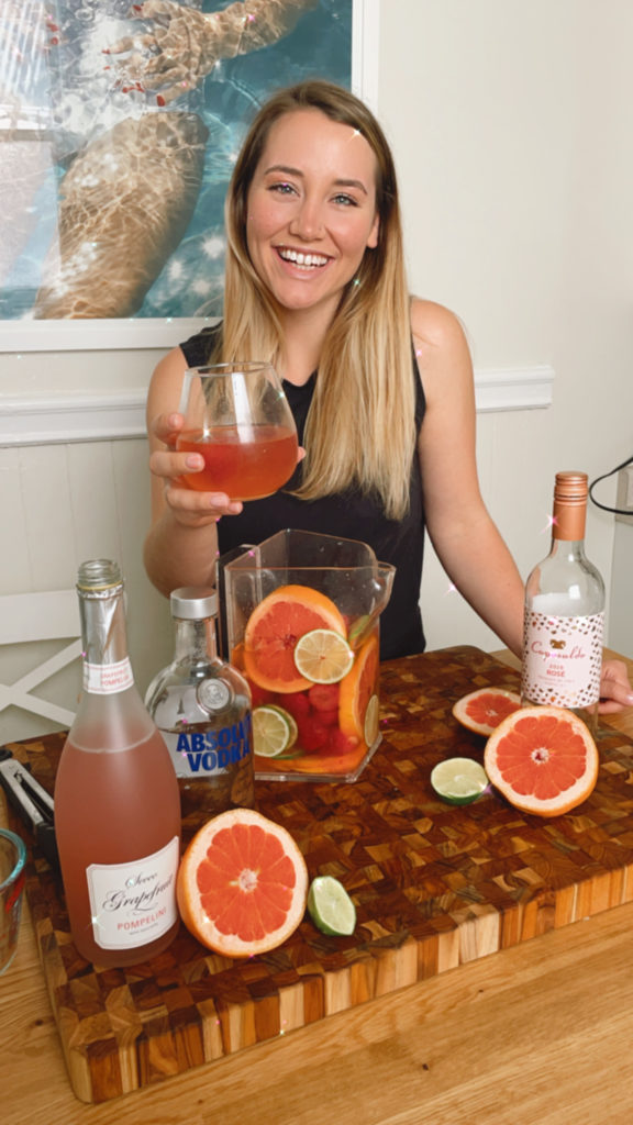 Girl smiling holding sangria in hand with sangria recipe ingredients on the table. 